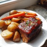A single serving of glazed mini meatloaf served with roasted potatoes and carrots on a white plate.