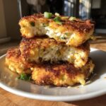A stack of three crispy, golden brown mashed potato cakes, one cut open to show the fluffy interior and green onions.