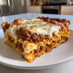 A thick, layered slice of homemade lasagna featuring rich meat sauce, creamy ricotta, and melted cheese topping.