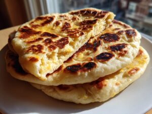 Close-up of a stack of freshly made homemade naan bread, brushed with butter and showing charred spots.