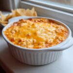 Close-up of hot buffalo chicken dip bubbling in a white ramekin topped with melted orange cheddar cheese.