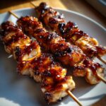 Close-up of three skewers loaded with juicy, grilled chicken skewers covered in a dark, sticky honey garlic glaze.