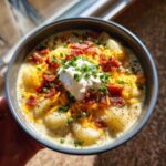 Close-up of a loaded bowl of creamy potato soup recipe topped with cheese, bacon, sour cream, and chives.