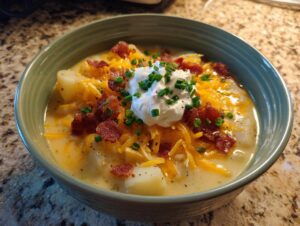 A close-up of a bowl of creamy potato soup recipe topped with shredded cheddar, bacon bits, sour cream, and chives.