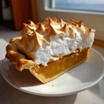 A close-up of a slice of rich, orange-filled butterscotch pie topped with dramatic, toasted meringue peaks.