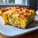 Close-up of a moist slice of Mexican cornbread, showing yellow cornmeal texture, melted cheese, and green jalapeño pieces.