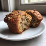 Close-up of two delicious banana nut muffins on a white plate, one cut in half showing the moist interior.