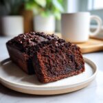 A thick slice of rich, dark chocolate banana bread topped with chocolate chips, ready to eat.