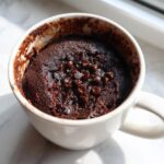 Close-up of a rich, dark chocolate chip mug cake baked inside a white mug.