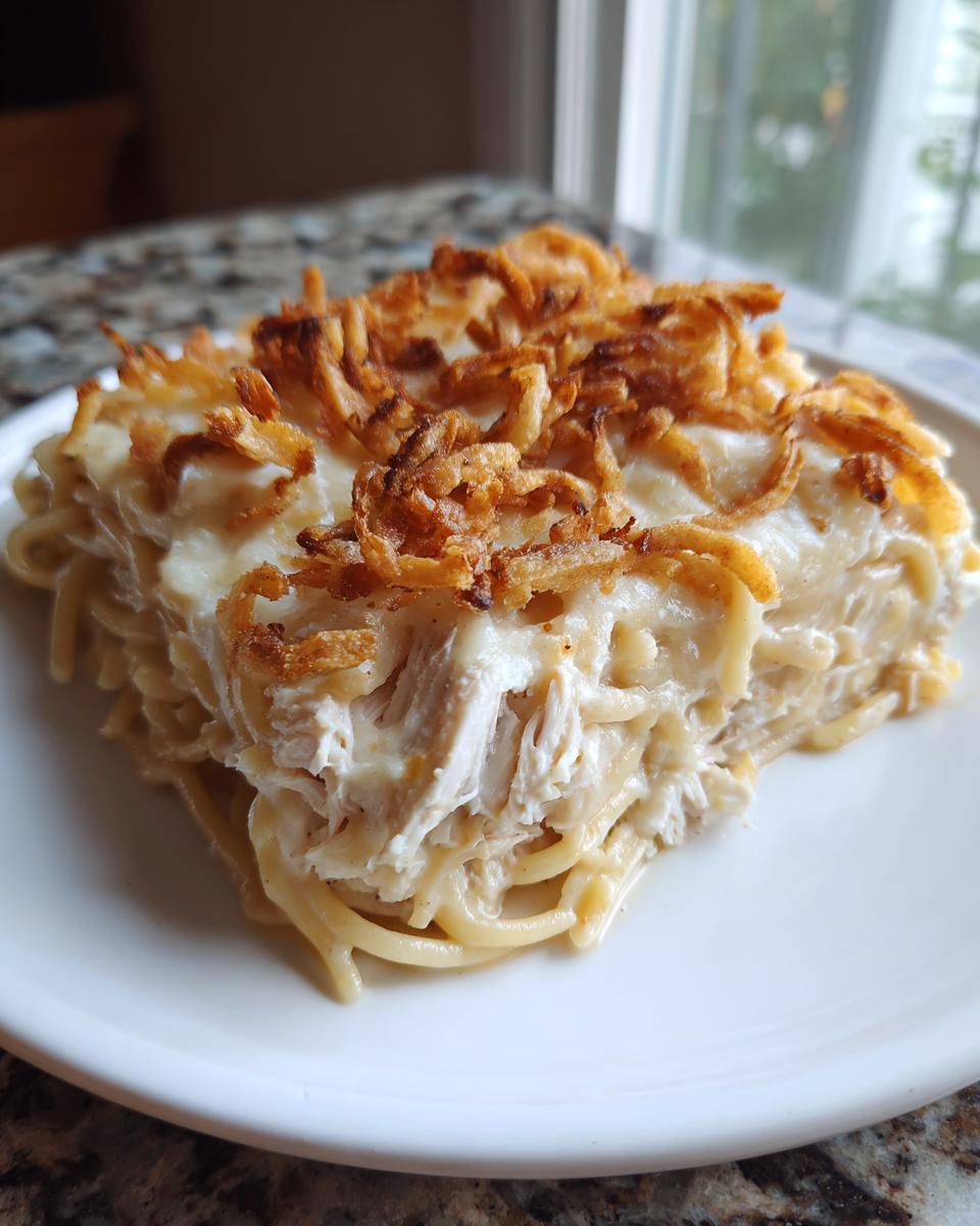 A square serving of creamy monterey chicken spaghetti topped with crispy fried onions on a white plate.