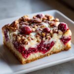 Close-up of a square slice of Nantucket cranberry pie featuring a thick cranberry layer, creamy filling, and pecan topping.