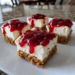 Four square no-bake cheesecake bites with a thick graham cracker crust and bright red strawberry topping.