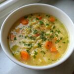 Close-up of a warm bowl of penicillin soup featuring broth, star-shaped pasta, sliced carrots, and fresh parsley.