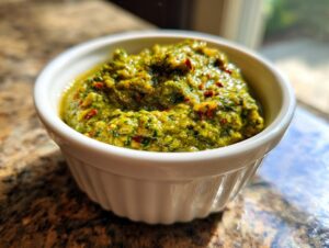 Close-up of vibrant green tomato salsa with red chili flakes served in a small white fluted ramekin.