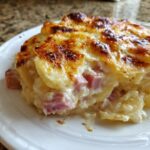 Close-up of a serving of scalloped potatoes and ham, showing creamy sauce, layered potatoes, and chunks of ham under a browned, cheesy crust.