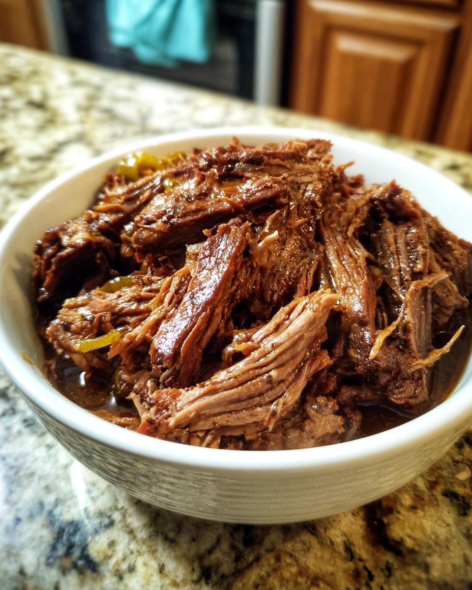 Close-up of tender, shredded Mississippi pot roast served in a white bowl on a granite countertop.