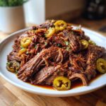 A mound of tender, shredded Mississippi pot roast topped with sliced pickled jalapeños and parsley.
