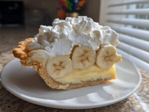 A close-up slice of banana cream pie showing the crust, creamy filling, banana slices, and a generous topping of whipped cream.