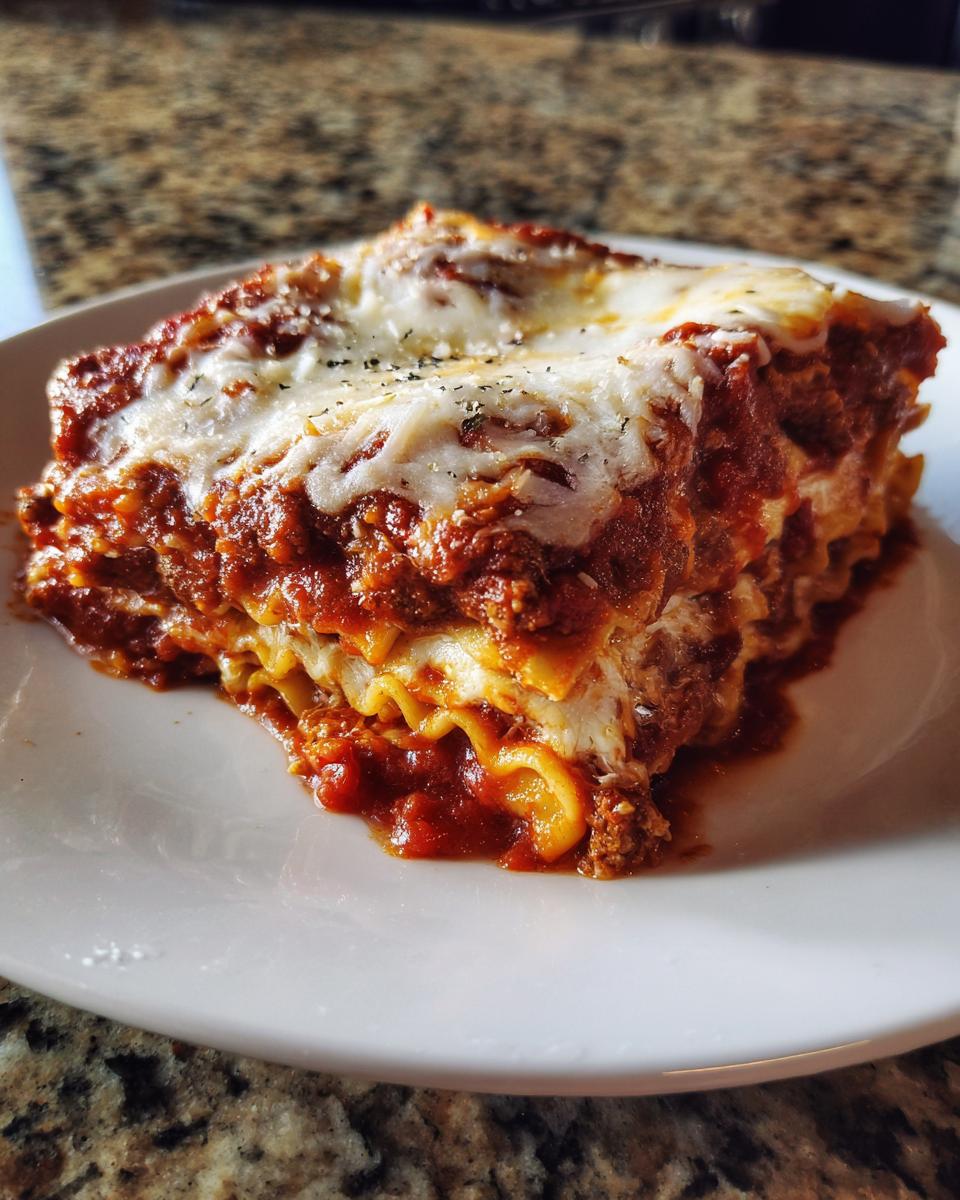 A thick, cheesy slice of baked ravioli casserole topped with melted mozzarella and herbs.