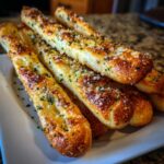 A close-up of several golden brown, soft breadsticks topped with melted butter, garlic, Parmesan cheese, and parsley.