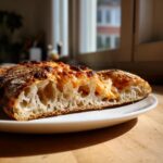 Close-up of a slice of pizza made with sourdough discard pizza dough showing a highly aerated, open crumb structure.
