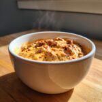 A close-up of a steaming hot sausage cheese dip in a white bowl, featuring melted cheese and crumbled sausage.