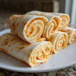 A stack of freshly made taco pinwheels showing the orange, creamy filling rolled tightly in tortillas.