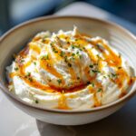A creamy bowl of whipped feta dip topped with golden honey drizzle and fresh chopped chives.