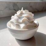 A small white bowl filled with perfectly piped whipped topping, likely for a dessert or savory dish accompaniment to the garlic sauce.