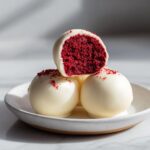 Close-up of white chocolate coated red velvet cake pops, one cut open to show the vibrant red interior.