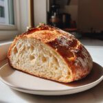 A close-up of a freshly baked artisan bread loaf, cut in half to show the airy crumb structure.