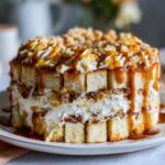 A tall, layered caramel apple trifle featuring cubes of sponge cake, whipped cream, and generous caramel drizzle.