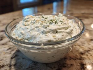Close-up of a creamy, chunky blue cheese dip garnished with herbs in a clear glass bowl.