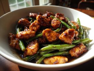 Close-up of delicious, glazed chicken and green beans served in a white bowl, ready to eat.