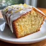 Close-up of a moist slice of lemon loaf topped with white glaze and lemon zest.