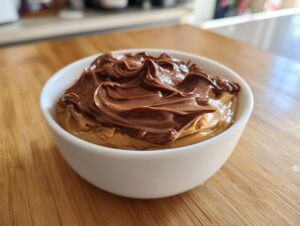Close-up of a white bowl filled with creamy peanut butter dip, topped with a generous swirl of chocolate spread.