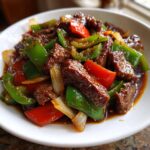 Close-up of tender beef strips and colorful bell peppers in a savory sauce, showcasing the finished pepper steak dish.