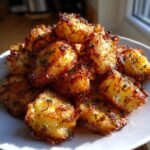 A pile of perfectly crispy, golden brown roast potatoes seasoned with herbs on a white plate.