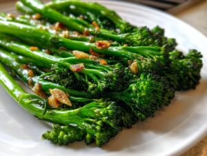 Close-up of bright green roasted broccolini spears seasoned with browned garlic pieces on a white plate.