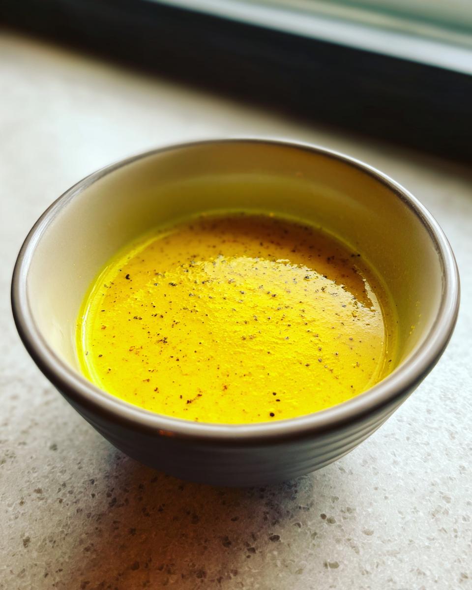 Close-up of bright yellow homemade salad dressing speckled with black pepper in a small bowl.