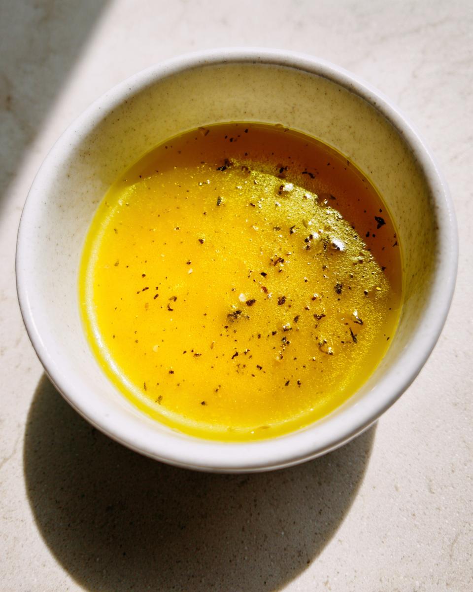 Close-up of a bright yellow homemade salad dressing seasoned with cracked black pepper in a small white bowl.