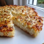 A slice of cheesy, herbed bread topped with melted cheese, likely made using a white pizza sauce base.