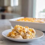 A serving of creamy chicken and rice casserole topped with melted cheddar cheese on a white plate.
