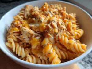 A close-up of a white bowl filled with creamy, cheesy chicken enchilada pasta made with rotini noodles and topped with melted cheddar.
