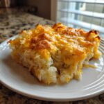 A close-up of a hearty slice of cheesy potato casserole topped with golden, melted cheddar cheese.