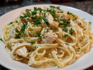 Close-up of a serving of rich chicken fettuccine alfredo pasta, topped generously with fresh parsley.