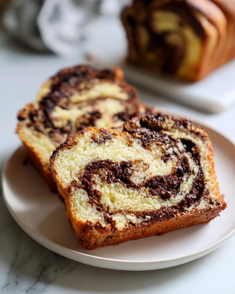 Two thick slices of homemade chocolate babka showing rich chocolate swirls served on a white plate.