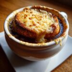 Close-up of a bowl of rich french onion soup topped with a thick layer of toasted bread and bubbly, melted Gruyère cheese.