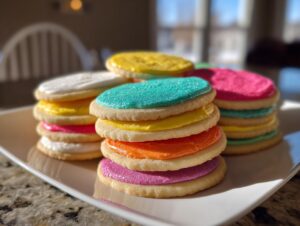 Stacks of colorful sugar cookies topped with smooth sugar cookie icing that hardens, featuring bright pink, yellow, orange, and turquoise colors.