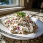 A mound of creamy cottage cheese chicken salad mixed with red onion and herbs, topped with fresh dill.